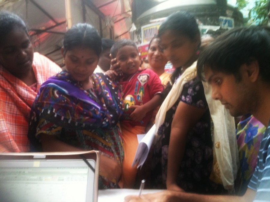 A KarmaCorps volunteer helping a family complete an RTE application on a laptop