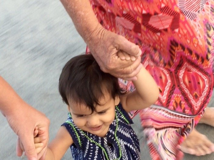 An elder and a parent holding a young child's hands